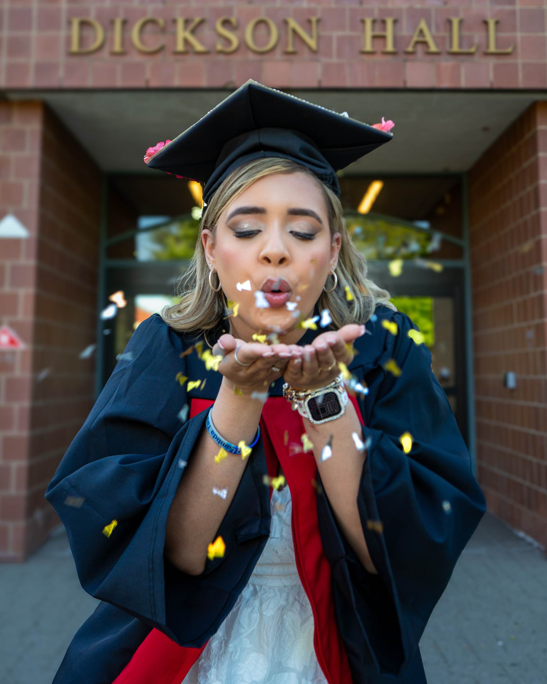 Graduate blowing confetti outside Dickson Hall