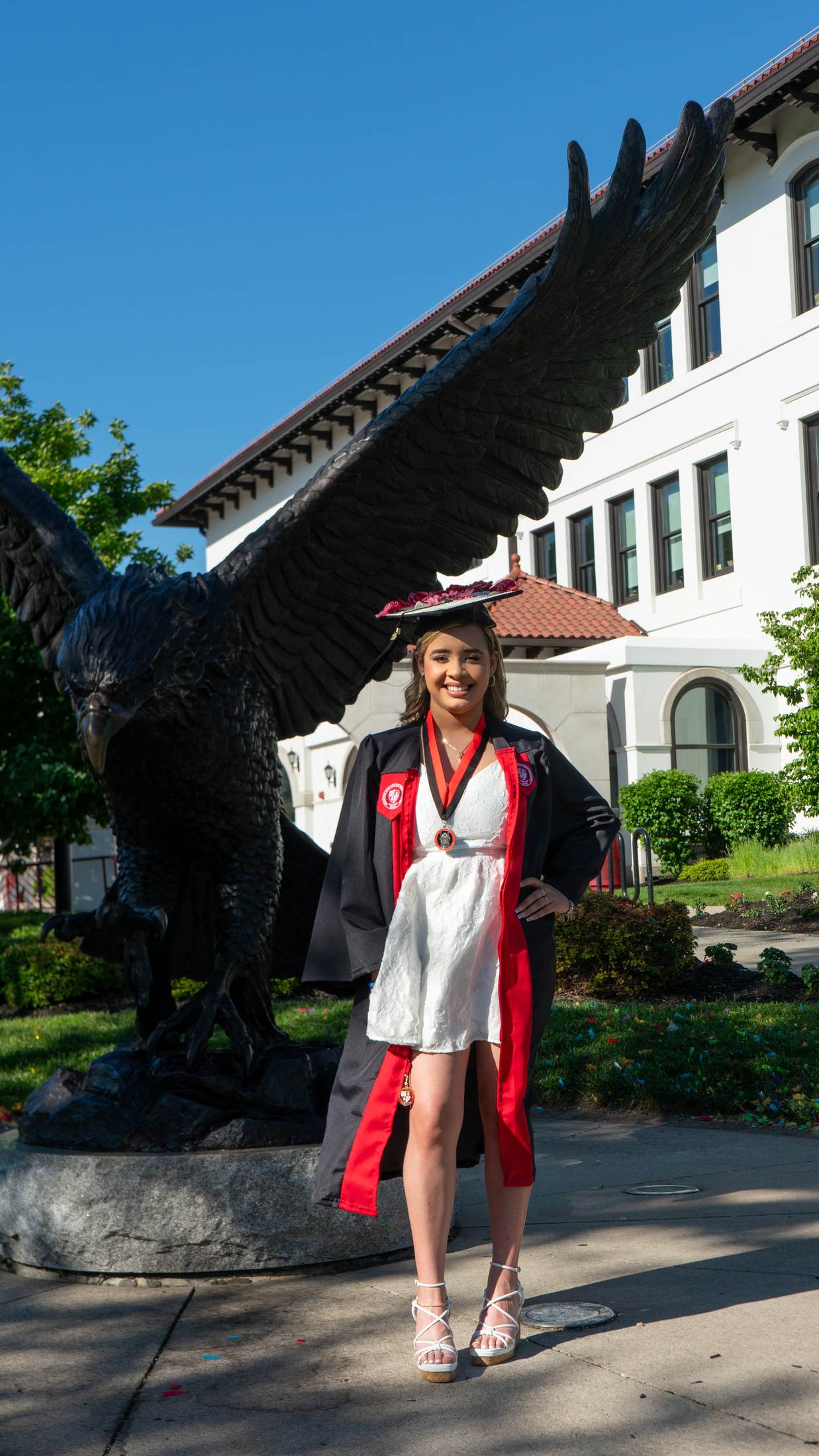 Graduate in cap and gown beside a campus eagle statue